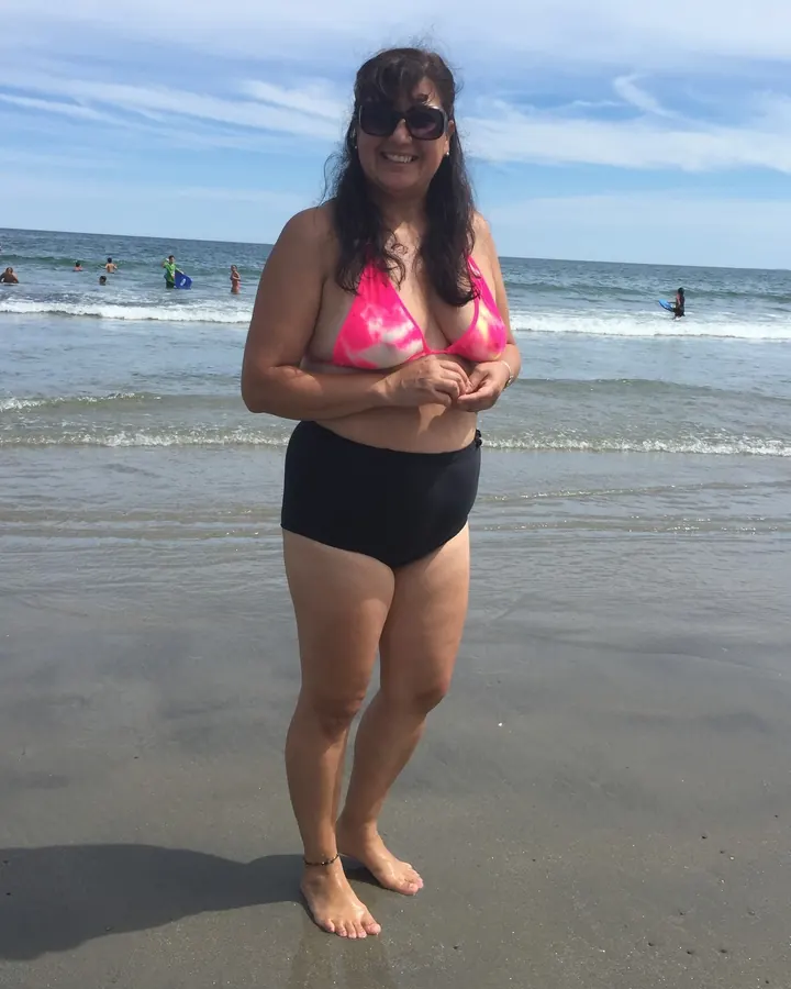 Femme en maillot de bain rose, sur une plage, souriant à l'appareil