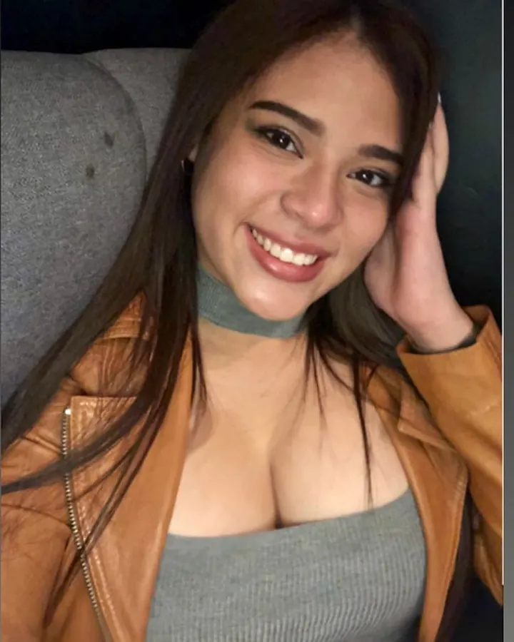 Femme asiatique souriante, en veste en cuir marron et haut gris, main sur la tête