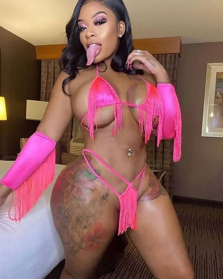 Femme nue, tatouage étoile sur l'épaule, prenant un selfie dans une salle de bain, regard direct.
