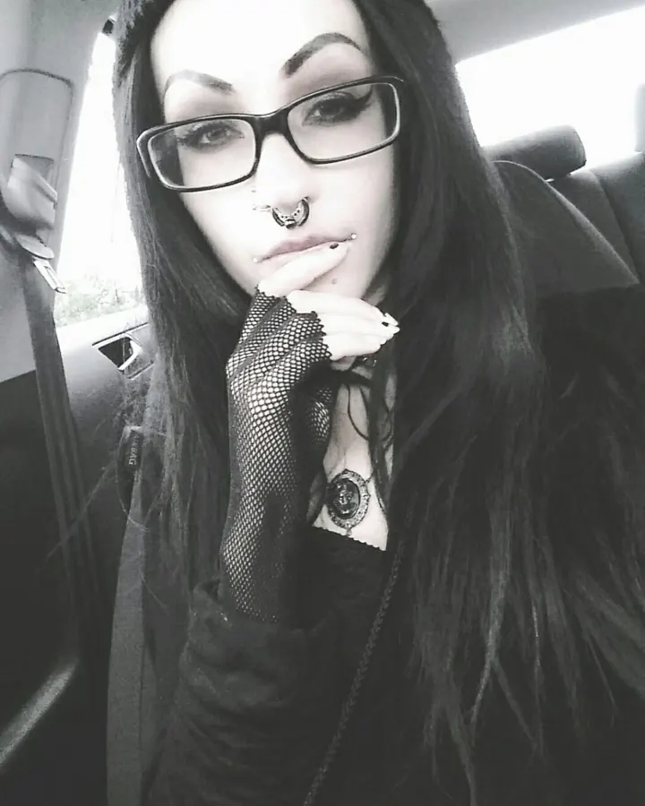 Femme aux cheveux longs noirs, portant des lunettes noires, un collier gothique et une manchette en maille, assise dans une voiture.