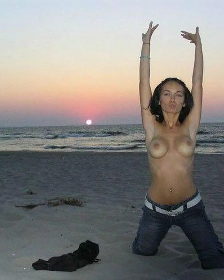 Femme indienne nue, genoux fléchis sur le sable, bras levés, au bord de la mer au coucher du soleil.