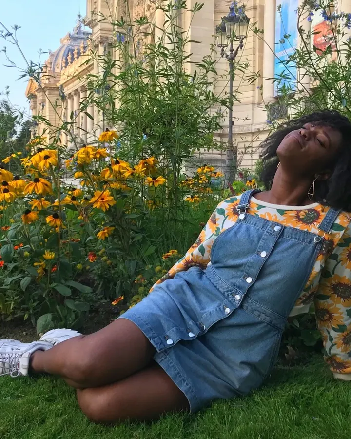 Femme aux cheveux bruns noirs portant un body rose, posant près d'une porte dans une chambre moderne