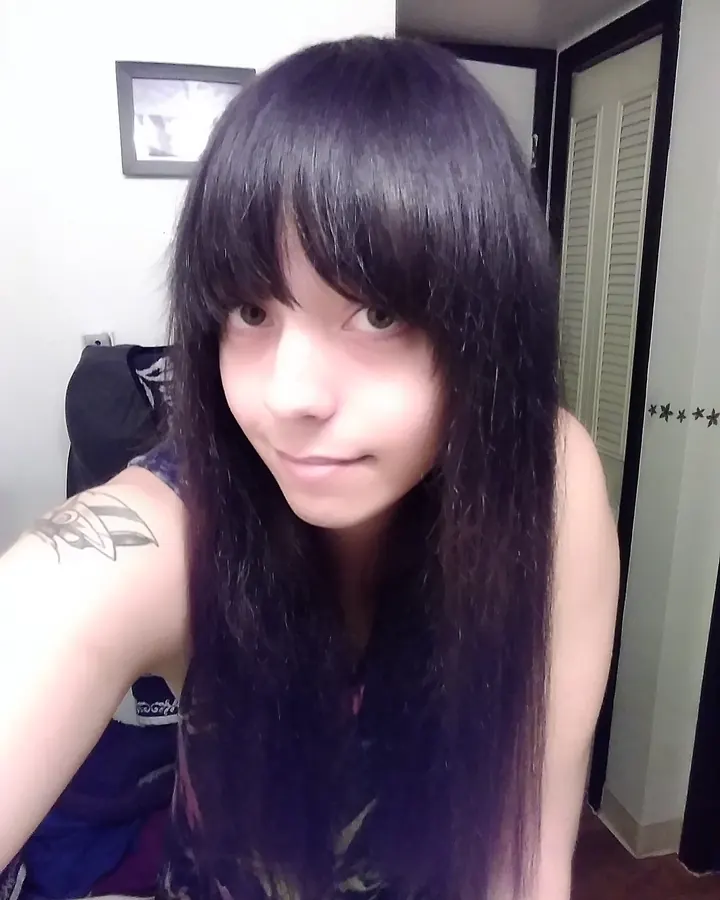 Femme latine aux cheveux bruns-noirs, en haut noir, posant sur un lit blanc.
