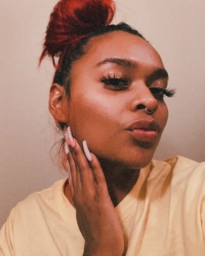 Femme aux cheveux roux coiffés en chignon, touchant son visage avec une main, regardant vers le bas.