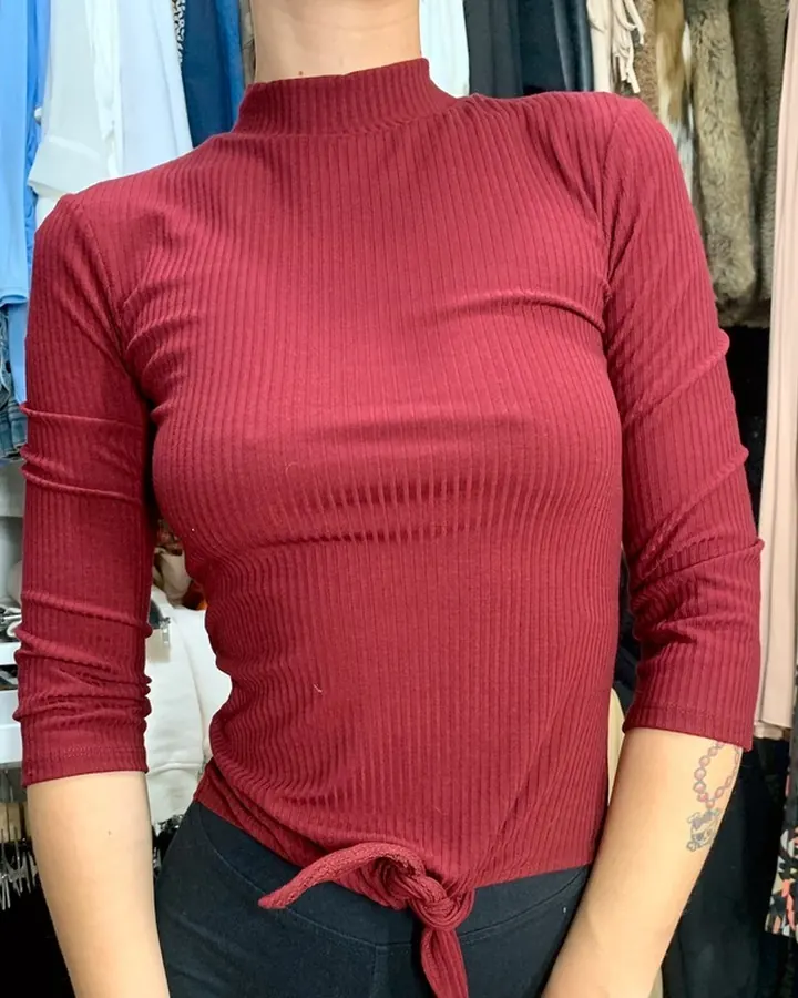 Femme portant un haut rouge à col montant, debout devant un armoire remplie de vêtements.