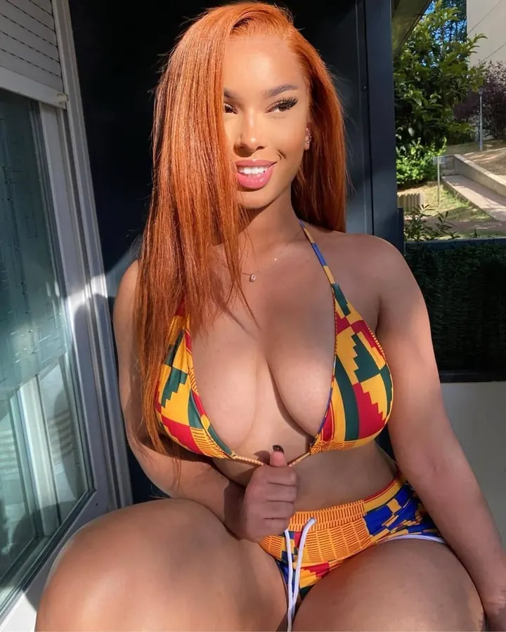Femme aux cheveux roux en maillot de bain coloré, assise sur un rebord ensoleillé.